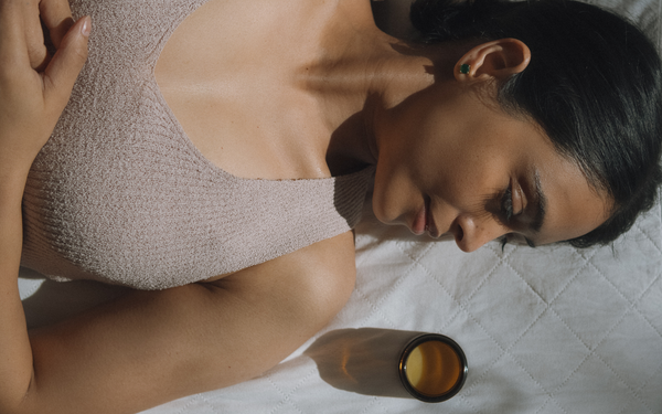 Woman resting on white linen beside a jar of Green Glow Universal Balm