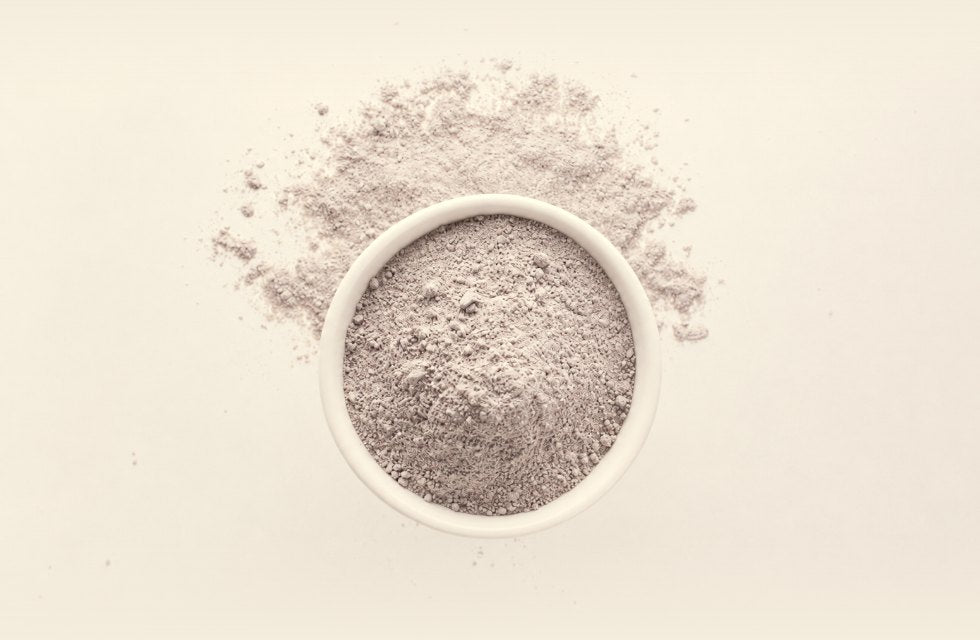 Glow Ubtan powder in a bowl with the loose botanical powder around it