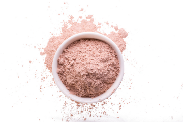A white bowl of fine pink clay powder spilling onto a white surface