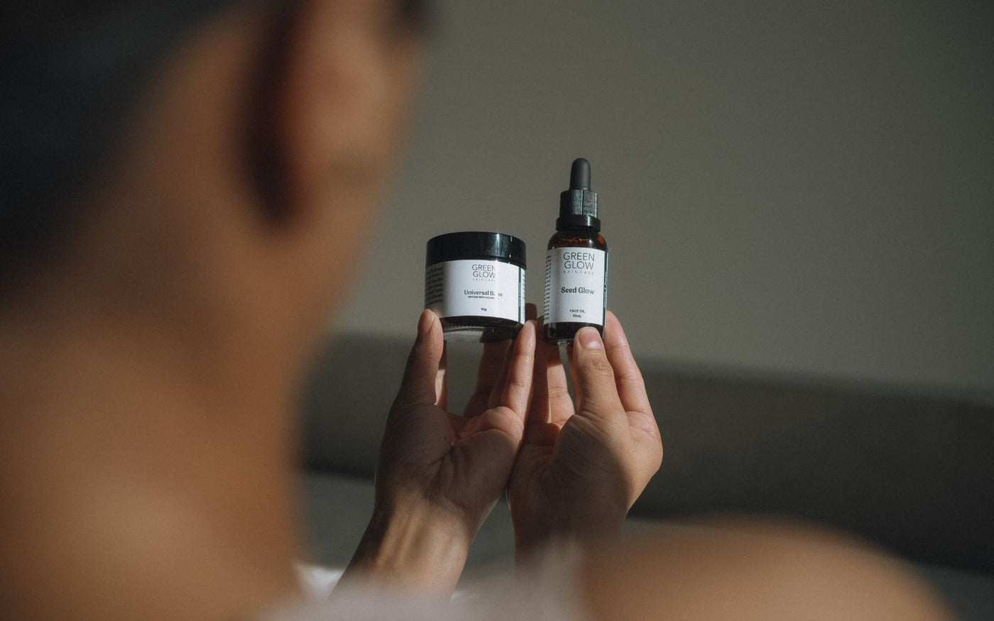 The 50g Universal Balm jar and the 30ml Seed Glow Face Oil bottle held up side by side to the light