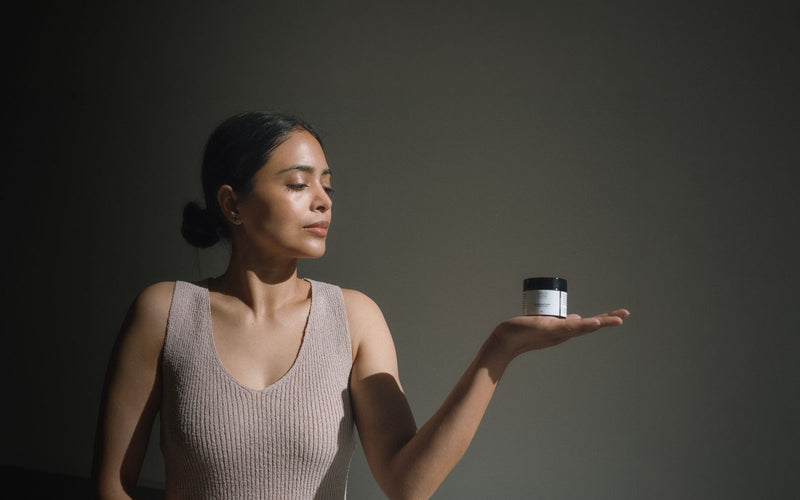 Green Glow founder Pooja holding the 50g Universal Balm jar on an open palm in a low, side-lit room