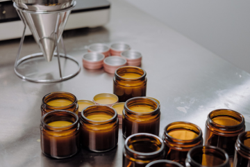Amber jars of freshly poured balm cooling on a steel bench, with lids stacked behind